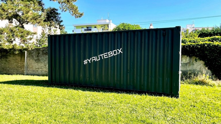 Container gris anthracite posé sur la pelouse dans un parc à annemasse ecrit yaute box en blanc