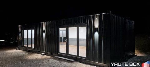 container ecole vue exterieur de nuit container foncé avec deux grande baie vitrées eclairées et des lumieres exterieurs eclairant en haut et en bas
