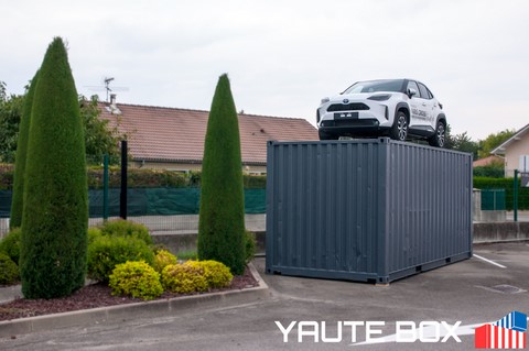 container chez toyota avec yaris sur le toit devant un bosquet vert de pin