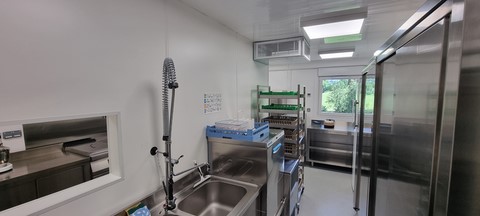 Intérieur de container cuisine avec des murs blanc en pvc vue sur un evier et un lave vaiselle professionnel